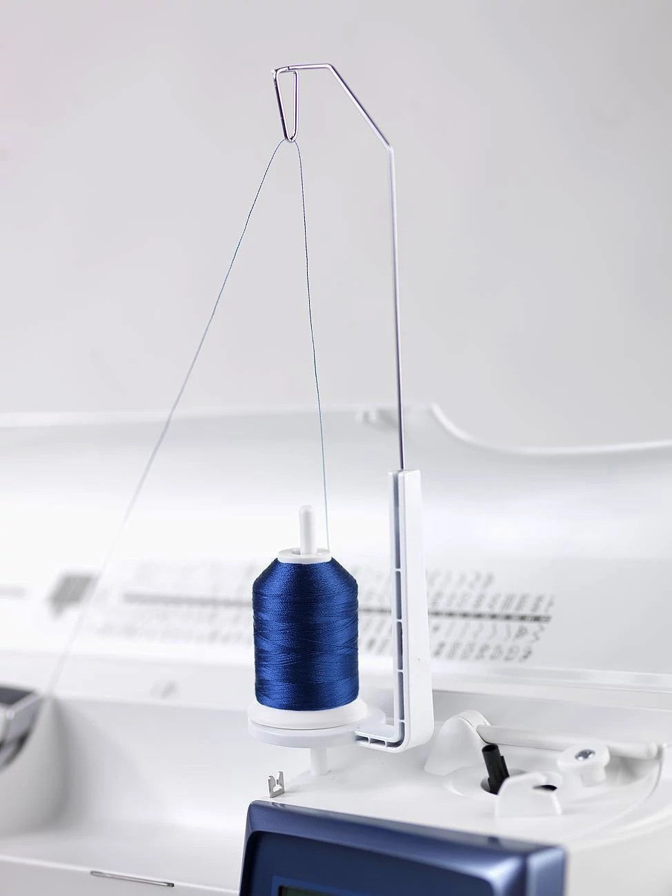 A blue spool of thread is mounted on a HUSQVARNA VIKING sewing machine spool stand, which is attached to the machine.