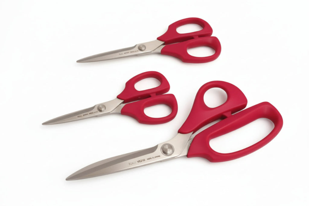 Three pairs of red-handled scissors on a textured fabric background