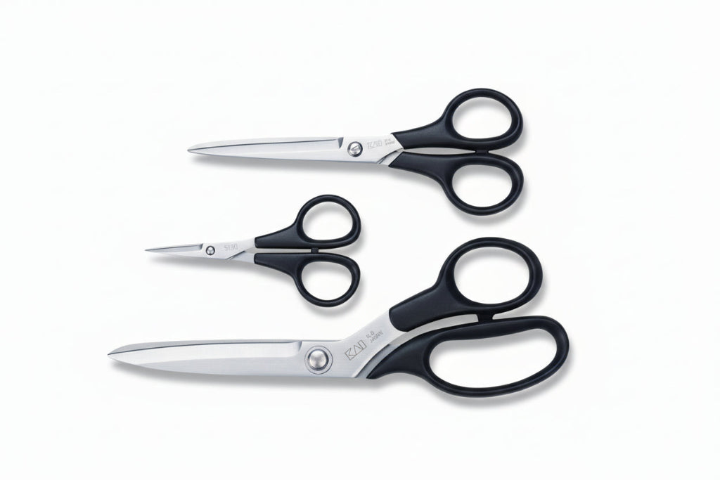 Three pairs of scissors with different sizes on a blue cutting mat with KAI branding.