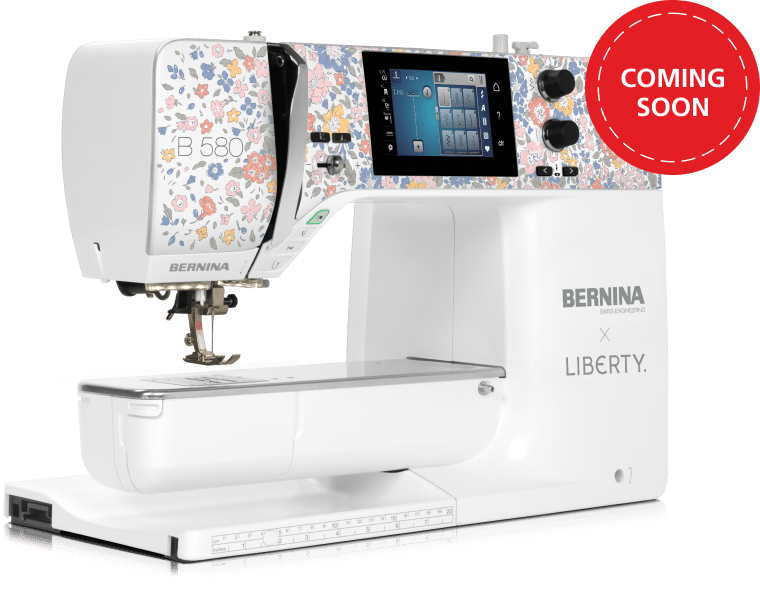 A BERNINA B 580 sewing machine with a white body, floral patterned upper housing, and a digital touchscreen display, shown on a solid green background with a red 'COMING SOON' badge in the top right corner.
